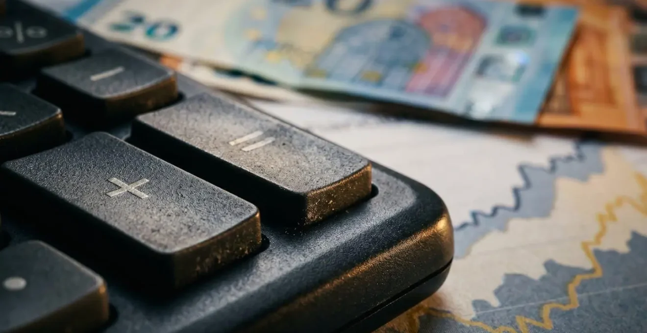 Calculatrice moderne posée sur des graphiques financiers avec des billets euros floutés en arrière-plan